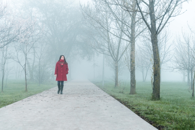 young woman in red walking by city park in fog in the morning